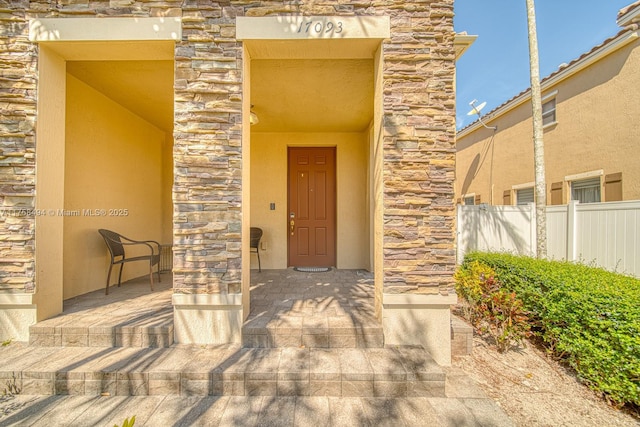 entrance to property with stone siding, fence, and stucco siding