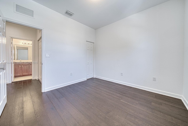 empty room featuring dark wood-type flooring, a sink, visible vents, and baseboards