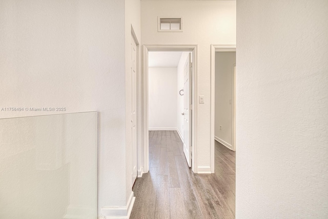 corridor with baseboards, visible vents, and wood finished floors