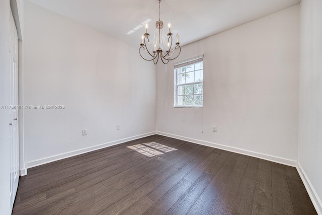 empty room with a chandelier, dark wood finished floors, and baseboards