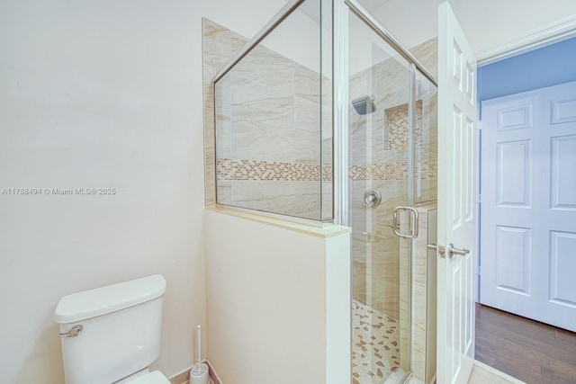 bathroom with a shower stall, toilet, and wood finished floors