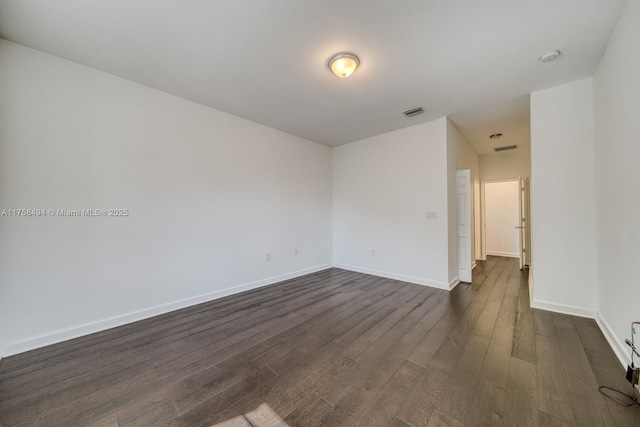 empty room featuring dark wood-style flooring, visible vents, and baseboards