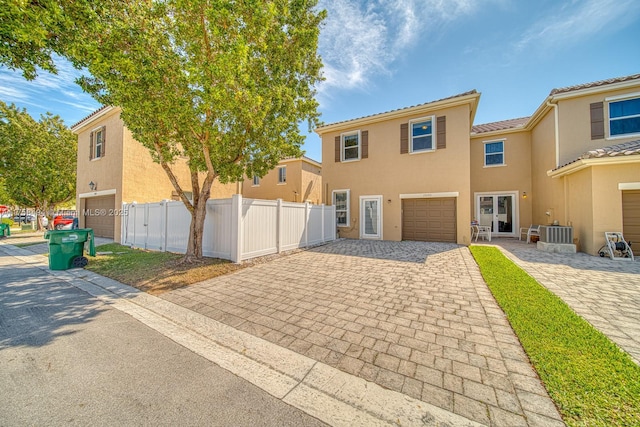 view of front of home featuring an attached garage, cooling unit, fence, decorative driveway, and stucco siding