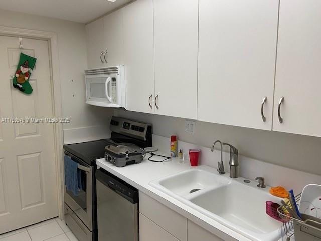 kitchen featuring light tile patterned floors, light countertops, appliances with stainless steel finishes, white cabinets, and a sink