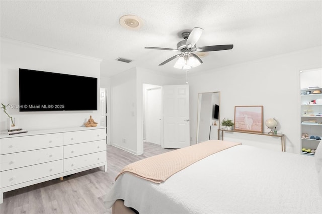 bedroom featuring a textured ceiling, light wood-style flooring, a ceiling fan, visible vents, and crown molding