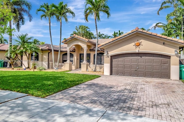 mediterranean / spanish house featuring a fenced front yard, a front yard, stucco siding, decorative driveway, and a garage