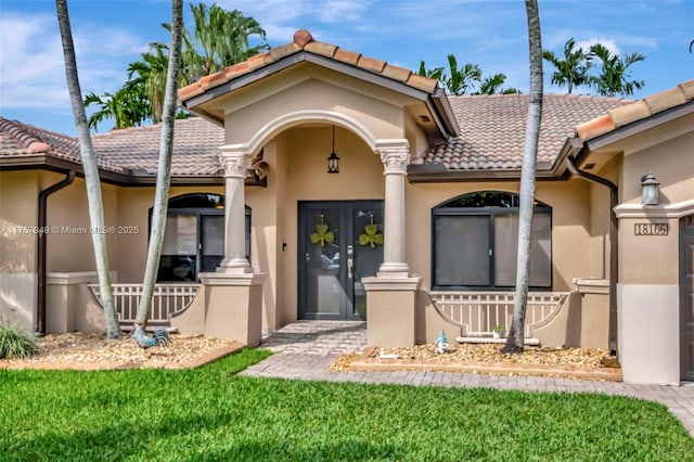 doorway to property featuring a tile roof, a lawn, and stucco siding