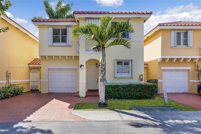 mediterranean / spanish-style home featuring a garage, decorative driveway, a tiled roof, and stucco siding