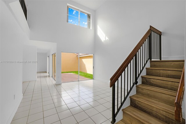 staircase with tile patterned floors, a high ceiling, and baseboards