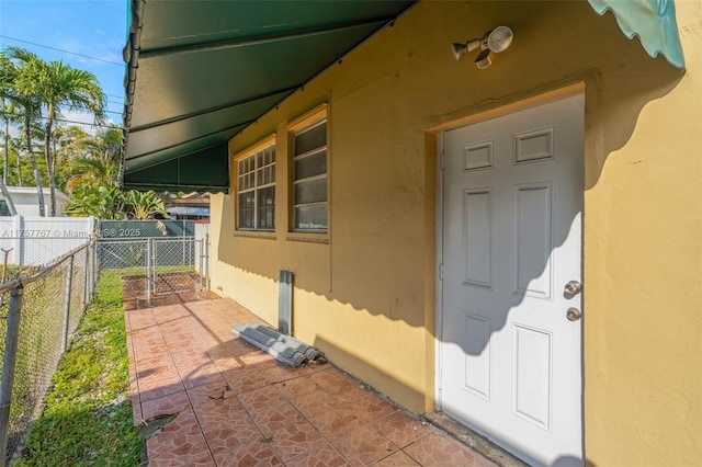 view of exterior entry with fence, a gate, and stucco siding