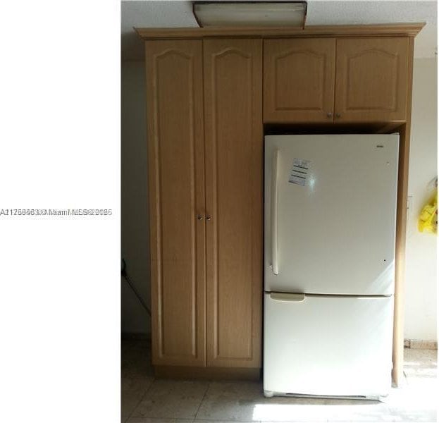 kitchen with light tile patterned floors, light brown cabinets, and freestanding refrigerator