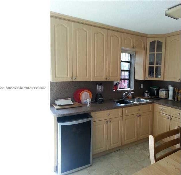 kitchen featuring light brown cabinets, a sink, decorative backsplash, glass insert cabinets, and fridge