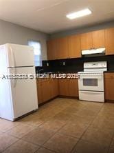 kitchen with under cabinet range hood, white appliances, and dark countertops