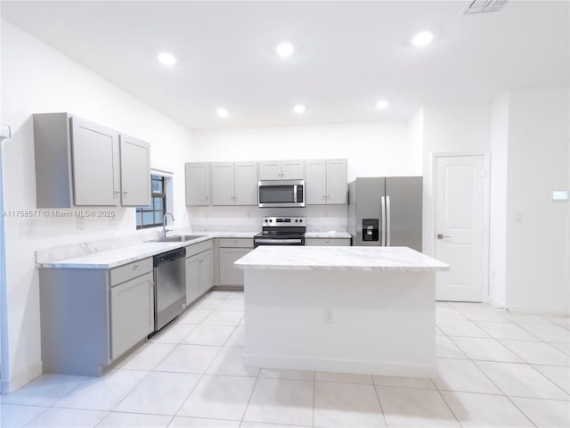 kitchen with recessed lighting, gray cabinetry, stainless steel appliances, a sink, and a center island