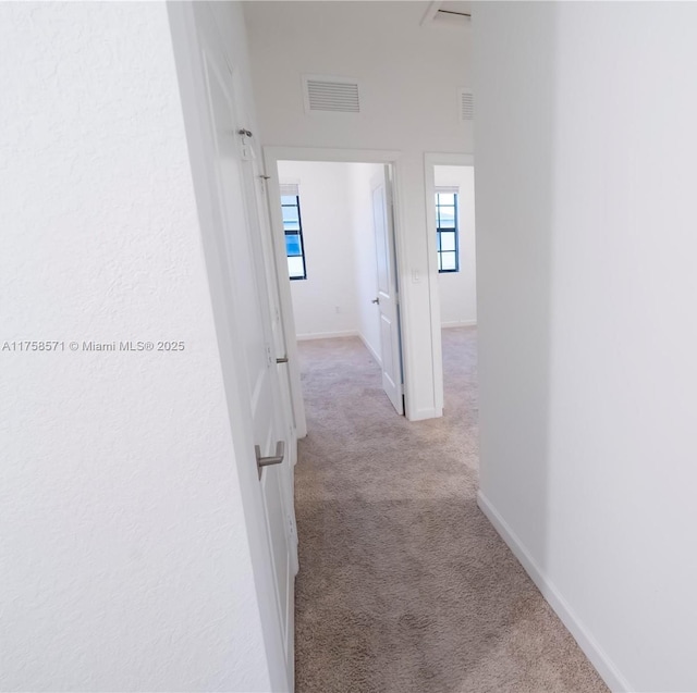 hallway featuring baseboards, visible vents, and carpet flooring