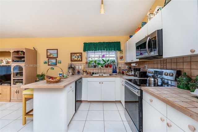 kitchen featuring light tile patterned floors, a peninsula, a sink, electric stove, and stainless steel microwave