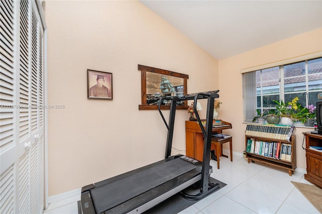 workout area featuring vaulted ceiling, light tile patterned floors, and baseboards