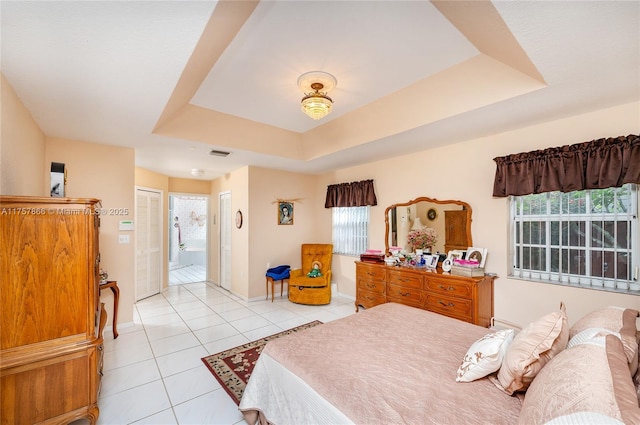 bedroom with a raised ceiling, visible vents, ensuite bathroom, and light tile patterned floors