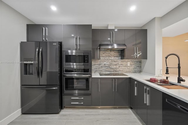 kitchen featuring gray cabinetry, under cabinet range hood, a sink, decorative backsplash, and black appliances