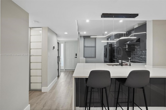 kitchen with light countertops, a sink, refrigerator with ice dispenser, light wood-type flooring, and a peninsula