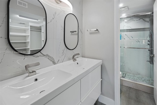 bathroom with toilet, a sink, visible vents, a marble finish shower, and double vanity