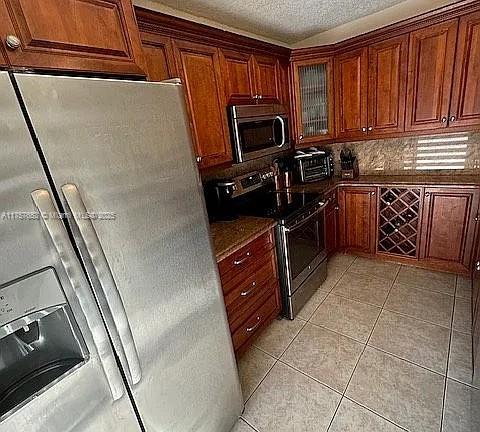 kitchen with tasteful backsplash, glass insert cabinets, light tile patterned floors, appliances with stainless steel finishes, and a textured ceiling