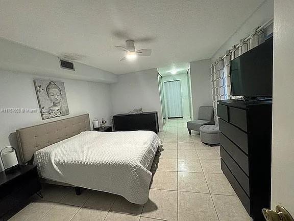 bedroom with light tile patterned floors, a ceiling fan, visible vents, and a textured ceiling