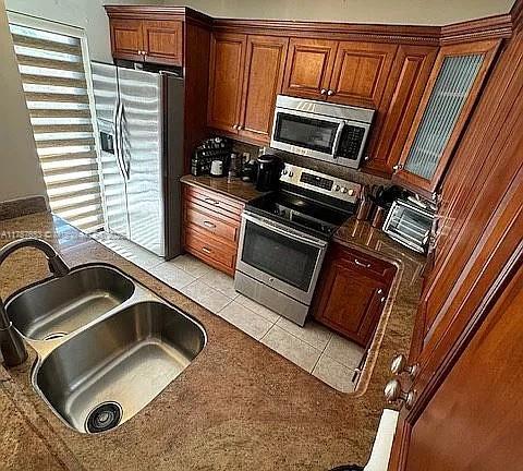 kitchen with light tile patterned floors, stainless steel appliances, dark countertops, and a sink