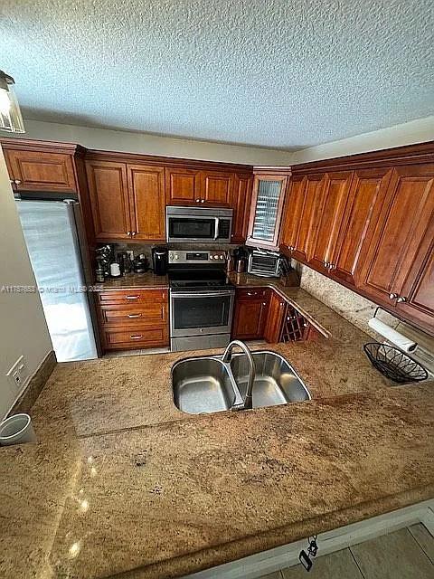 kitchen with a textured ceiling, dark stone counters, appliances with stainless steel finishes, and a sink