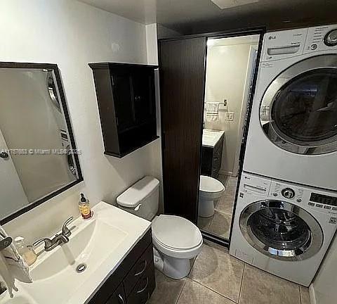 bathroom with tile patterned flooring, stacked washer / dryer, toilet, and vanity