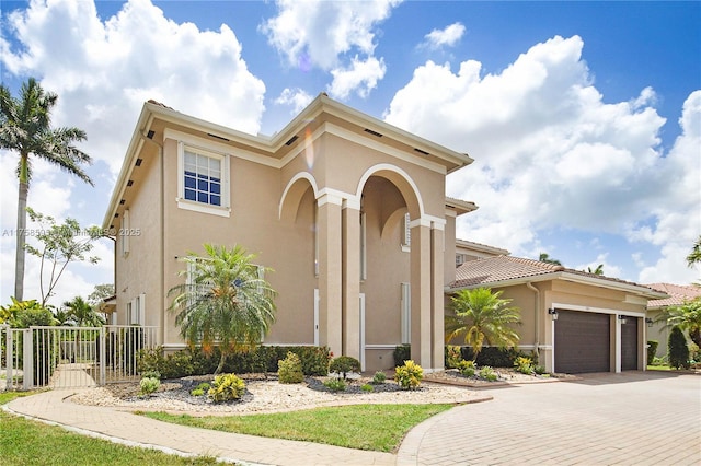 mediterranean / spanish-style home with decorative driveway, fence, an attached garage, and stucco siding