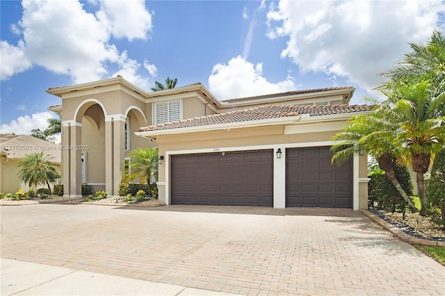 mediterranean / spanish-style home featuring a garage, decorative driveway, a tile roof, and stucco siding