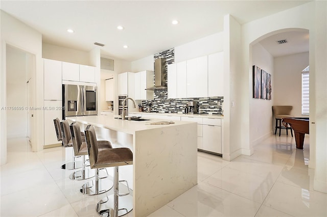 kitchen with a breakfast bar area, stainless steel appliances, visible vents, wall chimney range hood, and backsplash