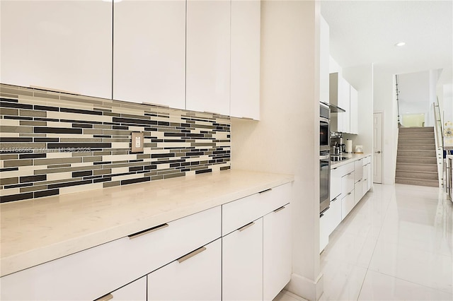 kitchen with white cabinets, modern cabinets, light stone countertops, stainless steel oven, and backsplash