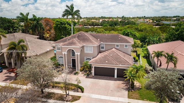 mediterranean / spanish-style house featuring a garage, a tiled roof, decorative driveway, and stucco siding