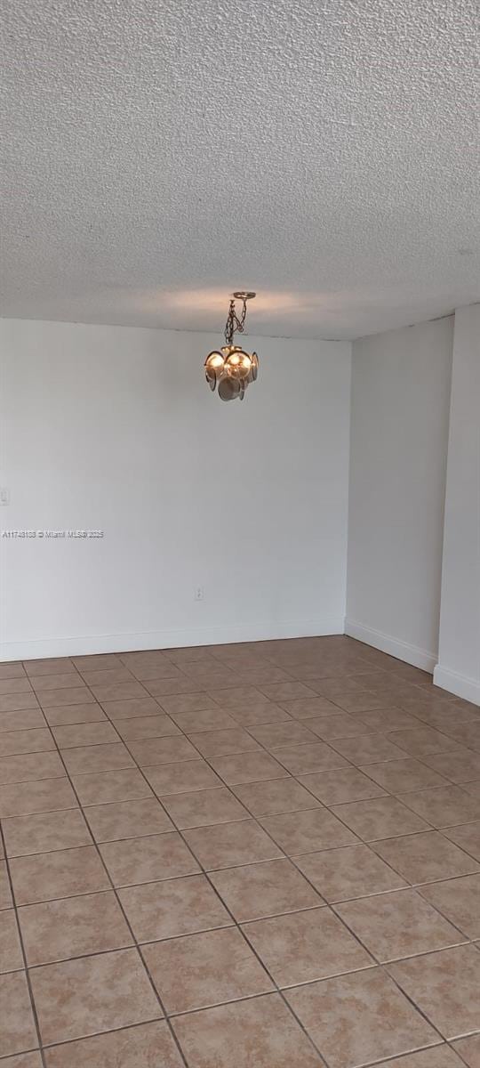 spare room featuring a notable chandelier, a textured ceiling, and baseboards