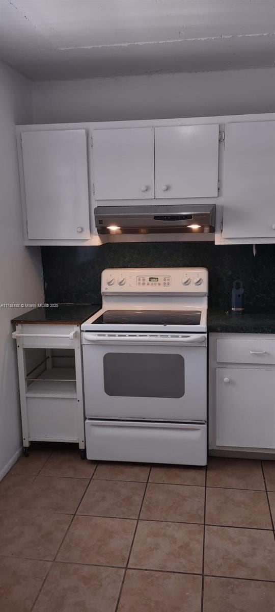 kitchen featuring dark countertops, white cabinetry, under cabinet range hood, and white electric range oven