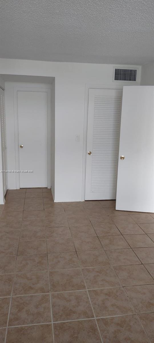 spare room featuring visible vents, a textured ceiling, and tile patterned floors