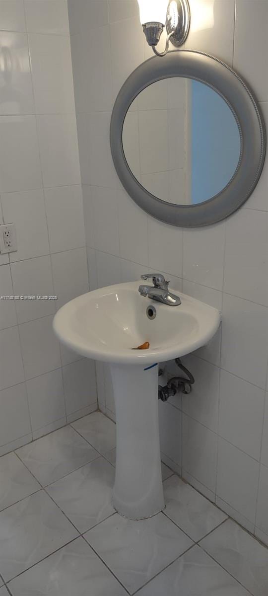 bathroom with marble finish floor, a sink, and tile walls