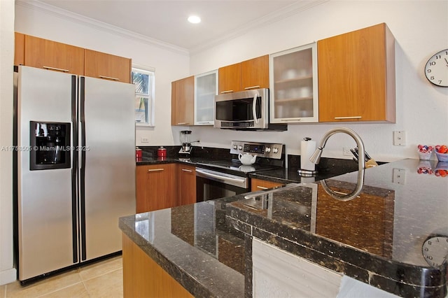 kitchen featuring crown molding, appliances with stainless steel finishes, brown cabinetry, glass insert cabinets, and dark stone countertops