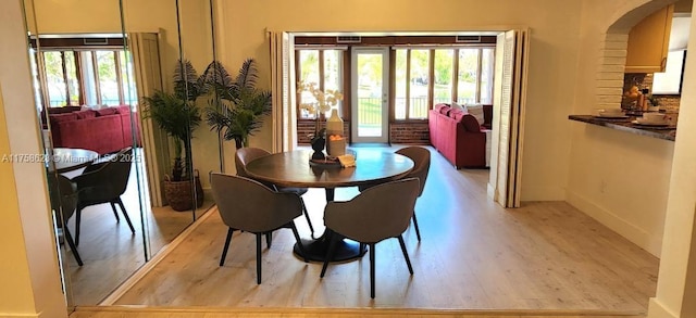 dining space featuring arched walkways, light wood-type flooring, plenty of natural light, and baseboards