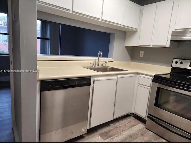 kitchen with under cabinet range hood, a sink, white cabinetry, light countertops, and appliances with stainless steel finishes