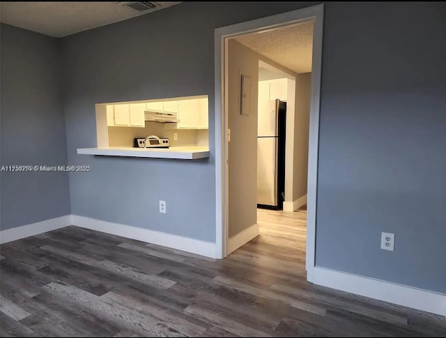 spare room featuring visible vents, a textured ceiling, baseboards, and wood finished floors