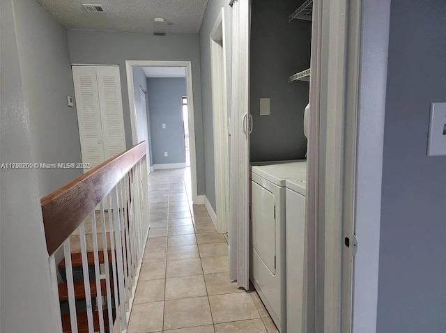 hall featuring washer and dryer, a textured ceiling, baseboards, and light tile patterned floors