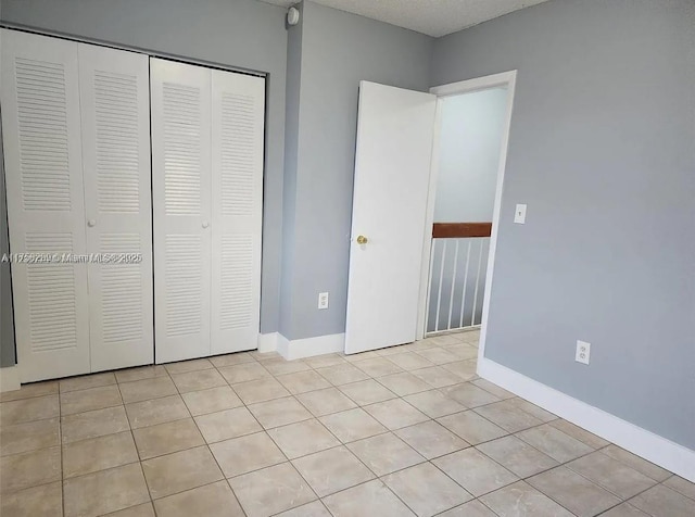 unfurnished bedroom featuring a closet, baseboards, and light tile patterned floors