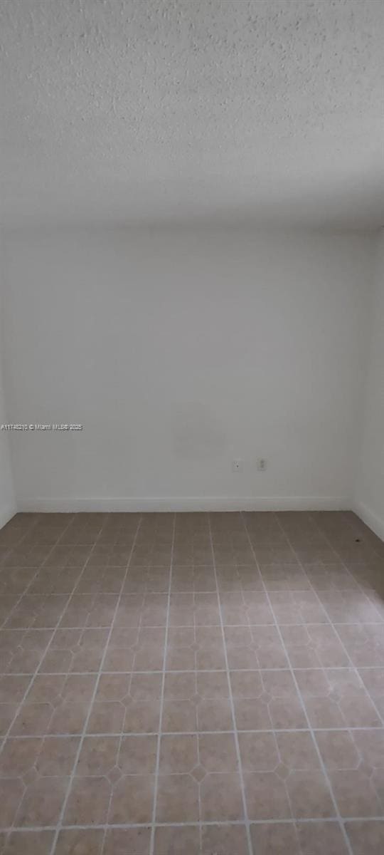 tiled empty room with baseboards and a textured ceiling