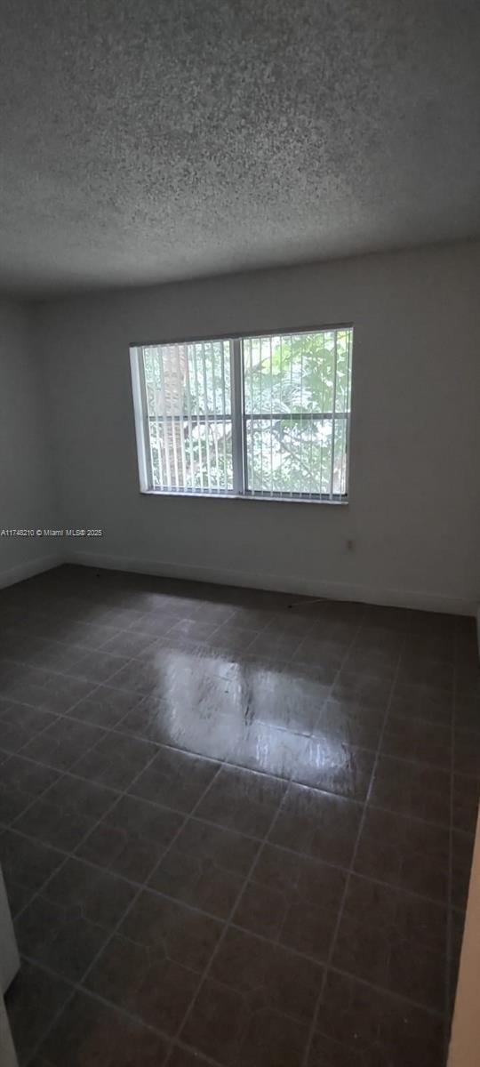 spare room with a textured ceiling, dark tile patterned floors, and baseboards