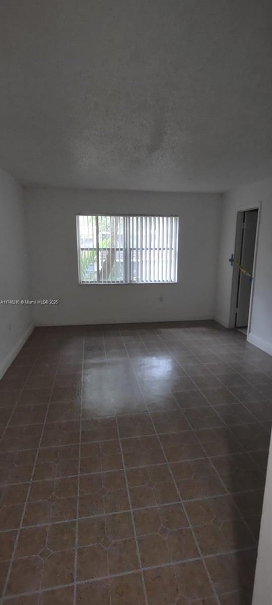 tiled empty room with a textured ceiling and baseboards