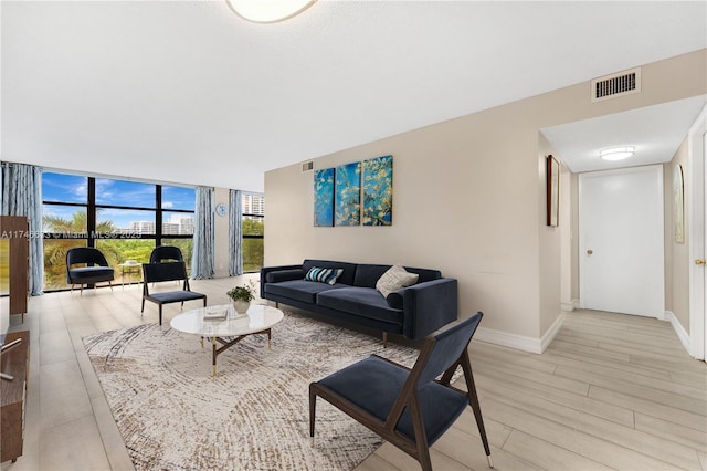 living area with a wall of windows, visible vents, light wood finished floors, and baseboards