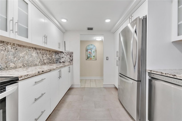 kitchen with stainless steel appliances, white cabinetry, backsplash, and light stone counters